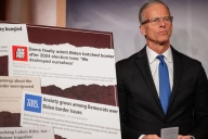 John Thune stands next to a poster of screenshots about the Democrats and border security