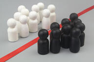 Groups of white and black people-like figurines are divided from one another by color, with a red line separating the two groups.