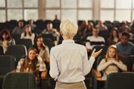 A photo from the back of a female professor teaching a lecture hall full of students.