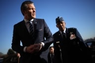 White man in suit in front of brown-skinned man in uniform