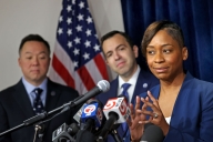 Massachusetts attorney general Andrea Campbell, in a navy blue blazer, speaks a podium topped with several microphones