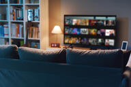 A photo of a relatively dark living room with the landing page for a streaming service visible on the TV, which sits next to a bookcase.
