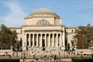 An image of the classical-style Low Memorial Library at Columbia University. Students can be seen sitting on its steps.