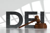 The acronym "DEI" in large black 3-D letters next to a judge's gavel.