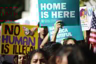 Students hold signs that read "no human is illegal" and "home is here."