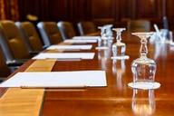 A photo of a wooden boardroom table, set up for a meeting, with pads of paper and water glasses. 