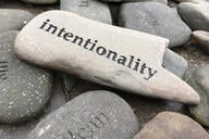 A photo of a pile of smooth stones, with the stone on top bearing the word “intentionality.”