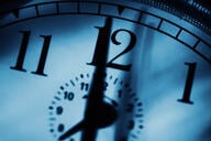 A close-up photo of a clock with a hand pointing to the 12.
