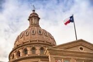 The dome of the Texas capitol, with the Texas state flag flying in front.