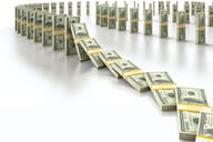 Stacks of $100 bills are lined up to mimic dominoes falling.