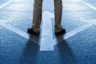 A photo of a man's legs standing on a set of painted arrows, pointing three different ways.