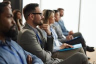 A row of five audience members participating in a seminar of sorts; all appear engaged by the content.