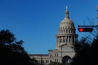 A photo of the Texas Capitol dome with a red stoplight in the foreground of the photo.