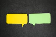 A photo of two speech bubbles, one yellow and one green, against a dark background.