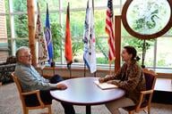Chris Caldwell, president of College of Menominee Nation, sits with a student on campus. They are at a round table sitting in front of various flags.