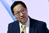 Santa Ono, an Asian man with black hair, wearing glasses and a dark suit with a yellow tie.