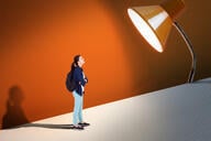 A student against an orange background with a spotlight shining down on them.