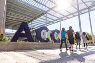 Students walk in front of a sign that reads "ACC" in large navy blue letters. 