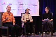 Three people are sitting in chairs on a stage participating in a panel discussion