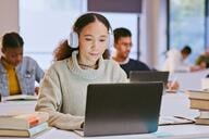 A student sits at a desk wearing headphones while typing on a laptop.