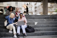Students sit on the steps near the college and look at the laptop and digital tablet and talk