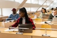 Young Black woman with long braids wearing a red plaid shirt taking a test at a laptop