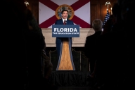 Ron DeSantis stands at a lectern that says "Florida The Education State," with the state flag behind him.