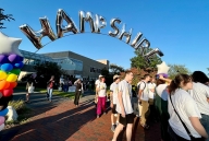 Students in white shirts walk beneath a large balloon arc, reading "Hampshire" in silver letters.