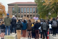 The backs of students holding signs outside of a large building.