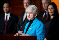 Virginia Foxx, a white woman with short white hair, stands at a podium in a blue blazer.