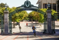 The gate at the entrance to the UC Berkeley campus, with a handful of people cycling and walking beneath it.