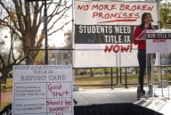 A student in a red sweater takes a podium at a Title IX protest in December