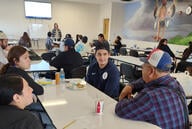 Students sit around a table talking with a Native American mural in the background.