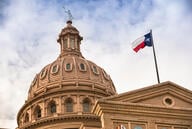 The dome of the Texas capitol, with the Texas state flag flying in front.