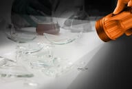 A flashlight shines a light on broken glass lab equipment. 