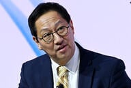 Santa Ono, an Asian man with black hair, wearing glasses and a dark suit with a yellow tie.