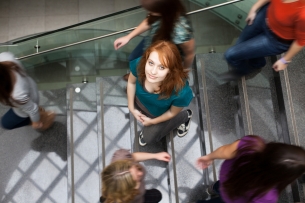 A student looks up as she walks on a busy staircase on a campus. 