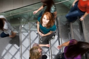 A student looks up as she walks on a busy staircase on a campus.