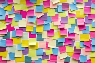 A white wall is covered in blank blue, purple, yellow, orange and green sticky notes.