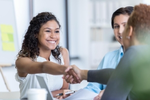 A young woman is shown in a business setting shaking hands with someone.