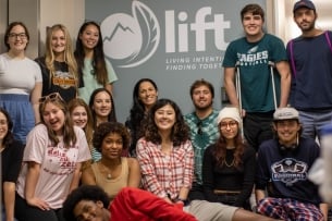 Students smile in front of a poster that features the LIFT logo and reads “LIFT, Living Intentionally, Finding Togetherness”