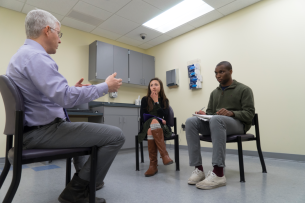 A professor sits with two students in a medical examiner room.