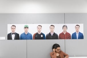 A viewer sits in front of an artistic work from Bayeté Ross Smith's "Our Kind of People" series, showing people in their own clothes on a white background.