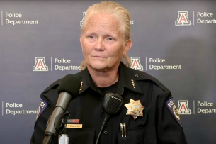 Paula Balafas, the now former chief of the University of Arizona Police Department, stands at a mic with the university logo on a wall behind her. She is a light-skinned middle-aged woman with blond hair.