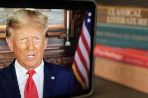A video of Donald Trump plays on an iPad with college textbooks in the background