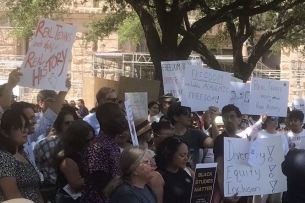 Dozens of people demonstrate holding up signs