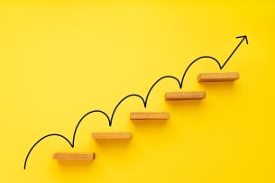 An arrow moving up five steps on a yellow background and pointing farther upward