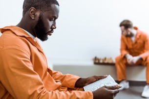 African American man wearing an orange jumpsuit reads a book.