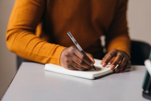 Hands and chest of a Black student writing in a notebook (opinion)