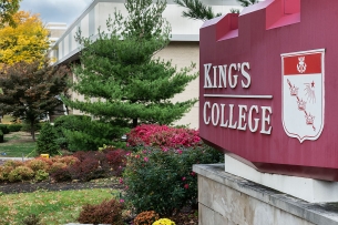 A red King's College sign beside some colorful shrubs.